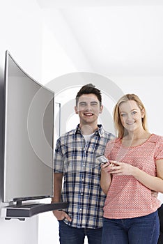 Portrait Of Young Couple With New Curved Screen Television At Ho