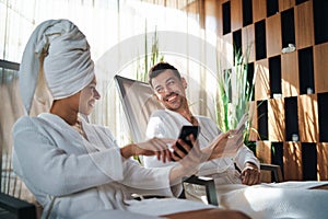 Portrait of young couple relaxing in spa resort, using smartphone.