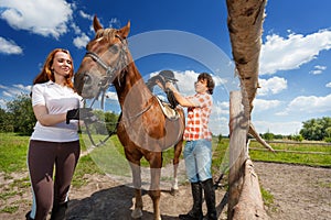 Portrait of young couple saddling their bay horse