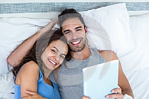 Portrait of young couple with tablet while lying on bed