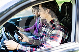 Portrait of a young couple texting while driving together on the road