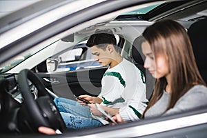 Portrait of a young couple use phones, texting and driving together, as seen through the windshield