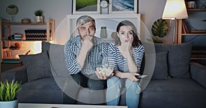 Portrait of young couple watching breaking news on TV at night expressing shock