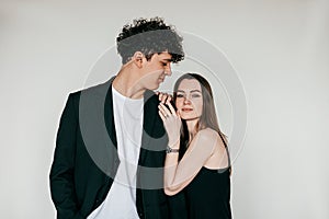 Portrait of young couple wearing black clothes. Young curly happy man looking at beautiful woman embracing shoulder.