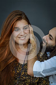 Portrait of a young couple where the young man with beard and long hair caresses the face of the young woman with long red hair