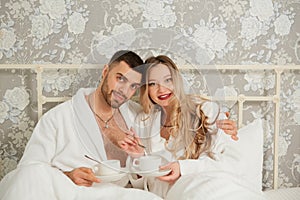 Portrait of a young couple in white coats drinking coffee in bed
