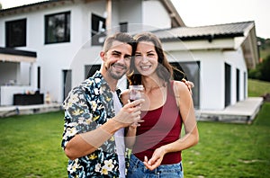 Portrait of young couple with wine outdoors in backyard, looking at camera.