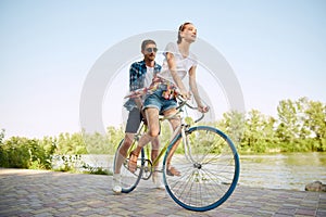 Portrait of young couple, woman and her boyfriend going for a bike ride in river enbankment on summer day. Romantic date