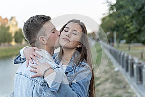 Portrait of young couple. Young man kissing his girlfriend outdoor. Gentle hugs on city backdrop. Romantic date