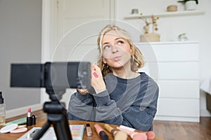 Portrait of young creative social media content creator, woman showing lipstick swatches on her hand, recording video