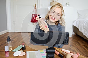 Portrait of young creative social media content creator, woman showing lipstick swatches on her hand, recording video