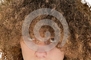 Portrait of a young curly European man with a serious look looking at his long hair with his eyes up. very lush male guy hair.