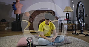 Portrait of young curly-haired boy wearing VR googles and talking. Cute Caucasian schoolboy in yellow T-shirt and blue