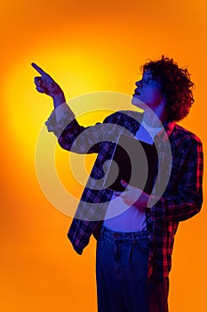 Portrait of young curly man in checkered shirt with tablet pointing right side with shocked expression isolated over