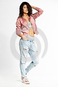 Portrait of young curly woman in jeans posing against white wall