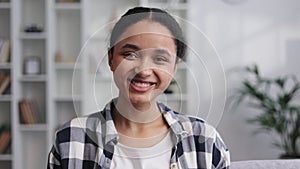 Portrait of a young cute African-American girl sitting on the sofa in the living room at home, turning her head to look