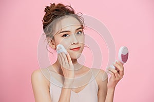 Portrait of young cute Aisan woman applying dry powder foundation makeup isolated over pink background photo