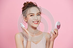 Portrait of young cute Aisna woman applying dry powder foundation makeup isolated over pink background