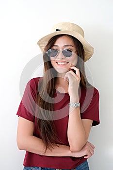 Portrait of young cute asian woman wearing sunglasses and hat smiling over white wall background