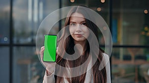Portrait of Young Cute Caucasian Lady Standing at Street in Front of Camera and Showing Smartphone with Green Screen