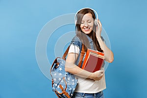 Portrait of young cute relaxed woman student in denim clothes with backpack headphones listen music, hold school books