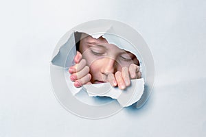 Portrait of young cute scared child girl  looking through a hole in the paper wall