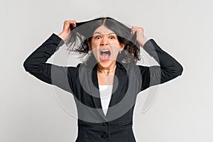 Portrait of young dark-haired girl in panic shouting and grabbing her hair in fear or frustration, standing in black blazer over