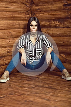 Portrait of young dark-haired model wearing skinny high-waisted jeans, striped tied up shirt, choker and golden sneakers