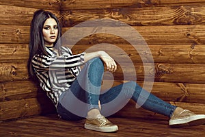 Portrait of young dark-haired model wearing skinny high-waisted jeans, striped tied up shirt, choker and golden sneakers