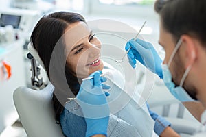 Portrait of young dentist in mask examining teeth of female client in the hospital