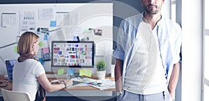 Portrait of young designer in front of laptop and computer while working. Assistant using her mobile at background.