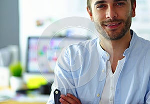 Portrait of young designer in front of laptop and computer while working. Assistant using her mobile at background.