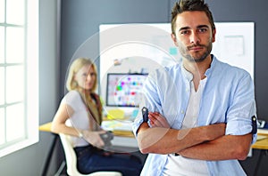 Portrait of young designer in front of laptop and computer while working. Assistant using her mobile at background.