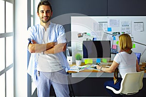 Portrait of young designer in front of laptop and computer while working. Assistant using her mobile at background.