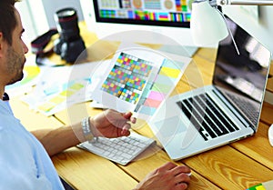 Portrait of young designer sitting at graphic studio in front of laptop and computer while working online.