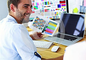 Portrait of young designer sitting at graphic studio in front of laptop and computer while working online.