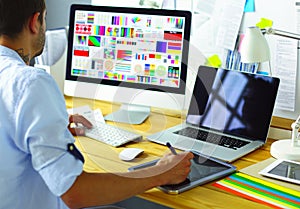 Portrait of young designer sitting at graphic studio in front of laptop and computer while working online.