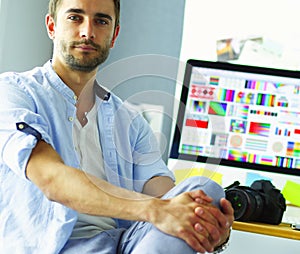 Portrait of young designer sitting at graphic studio in front of laptop and computer while working online.