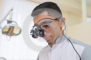 Portrait of Young doctor with dental binocular loupes on his face at dentist clinic.