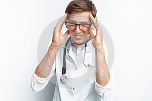 Portrait of a young doctor, on a white background, which depicts a headache, trainee in the Studio, with a stethoscope on the neck