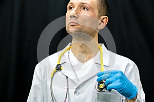 Portrait of a young doctor in a white coat on a black background. A doctor in blue gloves and with a medical stethoscope around