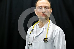 Portrait of a young doctor in a white coat on a black background. A doctor in blue gloves and with a medical stethoscope around