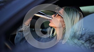 Portrait of young driver blonde girl inside car, drinking water from steel thermo eco bottle. Wearing hipster sunglasses.