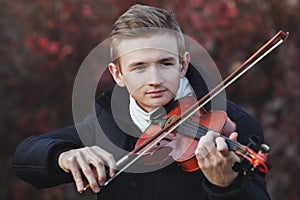 Portrait of a young elegant man playing the violin on autumn nature backgroung, a boy with a bowed orchestra instrument makes a