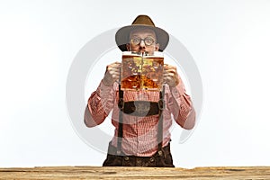 Portrait of young emotional man in hat, wearing traditional Bavarian clothes, holding beer mug isolated white background