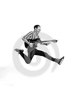 Portrait of young emotive man in stylish clothes playing guitar, posing isolated over white background. Black and white