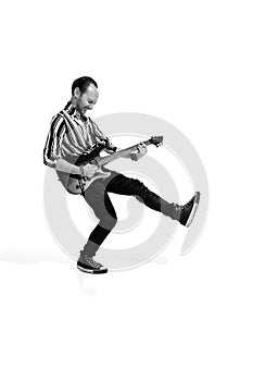 Portrait of young emotive man in stylish clothes playing guitar, posing isolated over white background. Black and white