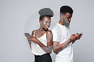 Portrait of young excited african couple with mobile phone spy each other isolated on gray background