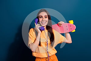 Portrait of young excited lady invited by friends calling telephone to ride skate together in park isolated on dark blue