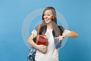 Portrait of young excited smiling woman student with backpack holding school books pointing index finger on copy space